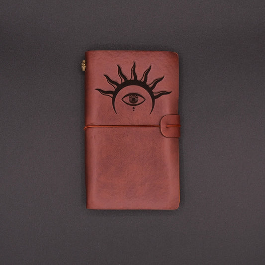Brown, vegan leather vintage diary with an hermetic eye engraved on it, over a black background.