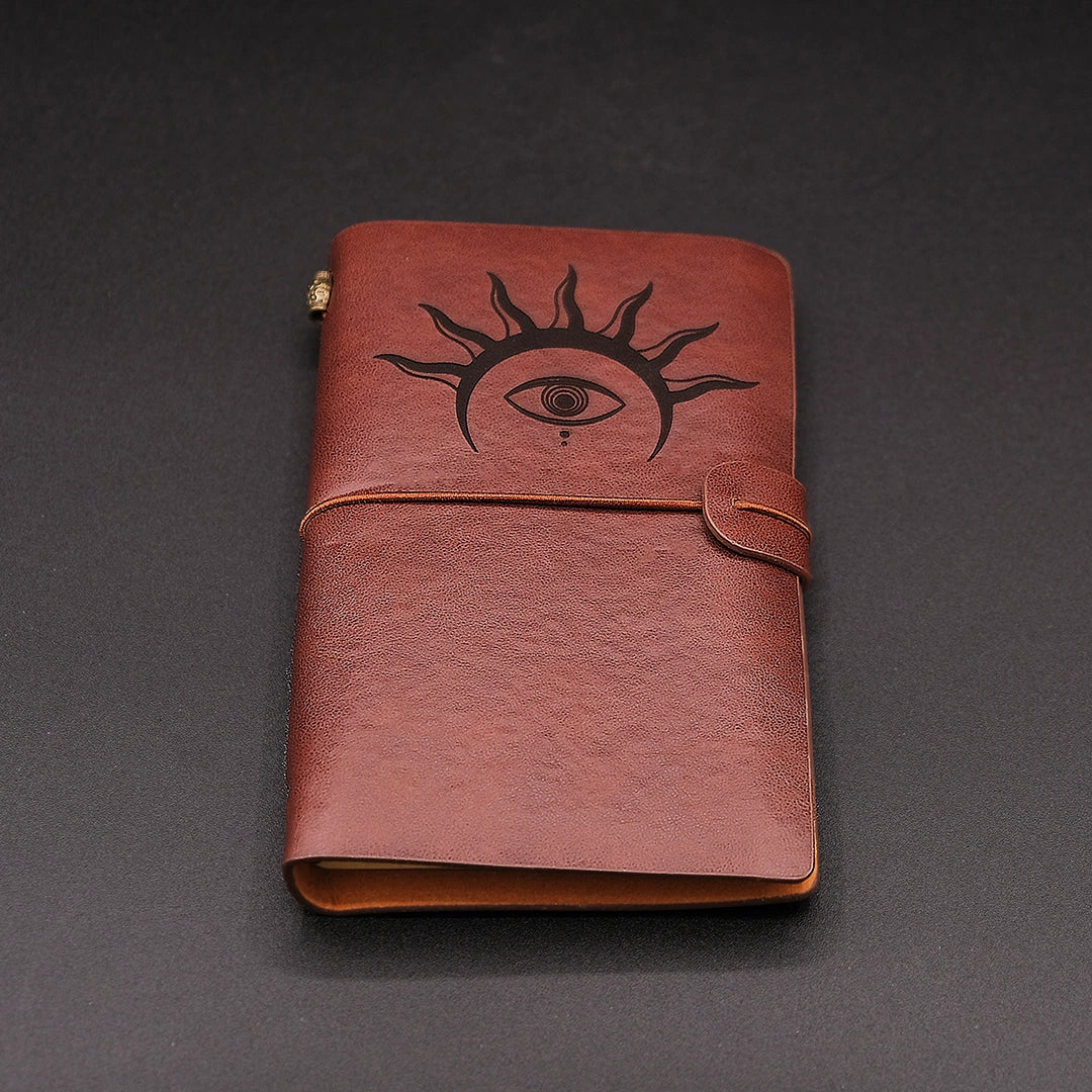 Brown, vegan leather vintage diary with an hermetic eye engraved on it, over a black background.
