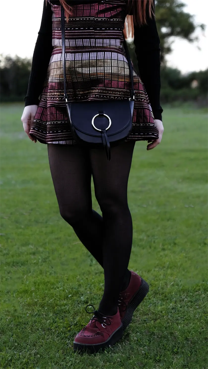 A girl wearing a red and golden dress is posing with a black leather bag decorated with a golden ring and a slavic pattern