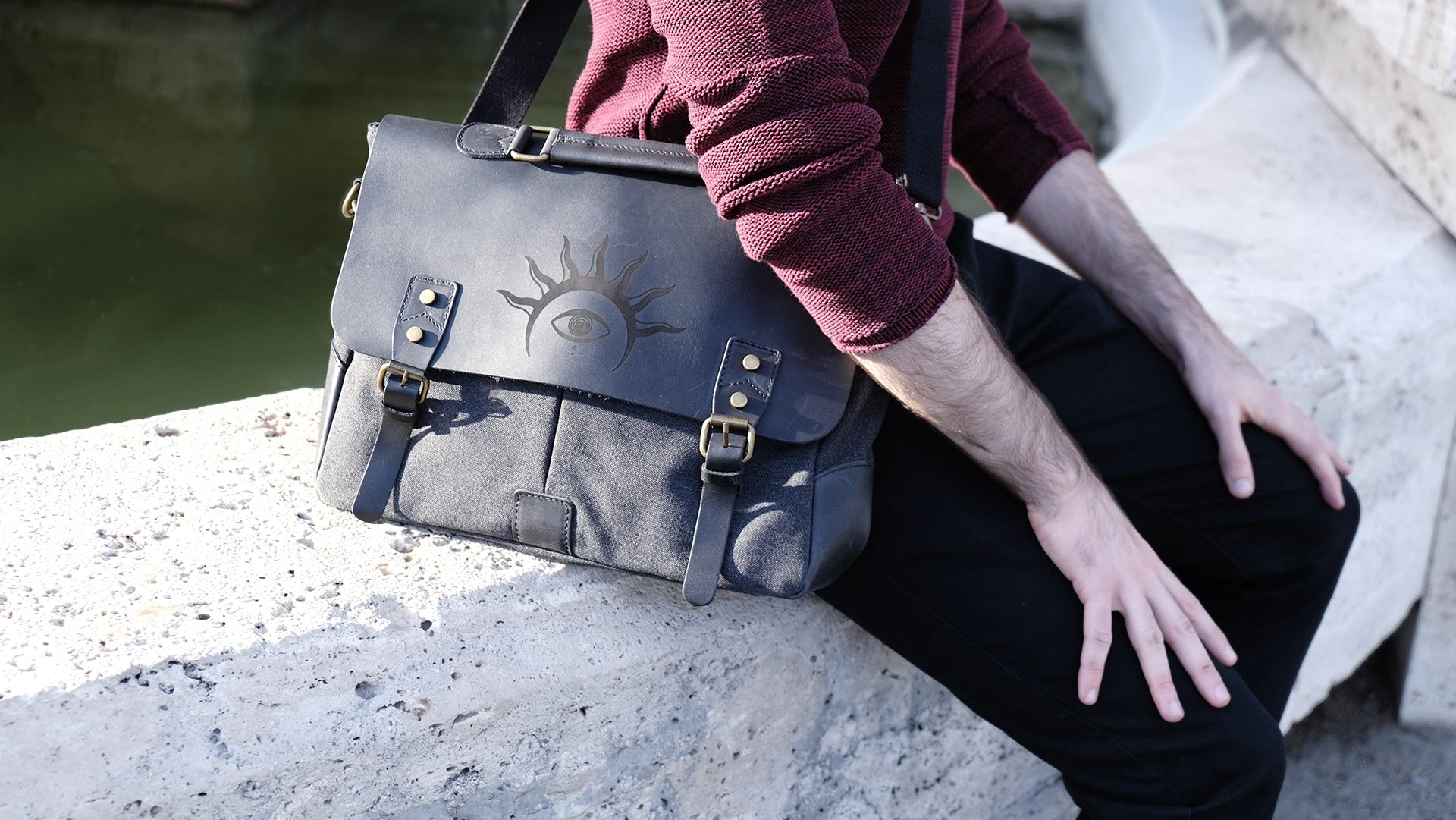 A model is wearing a black leather satchel engraved with a mystic eye with a solar crown. Dark academia style