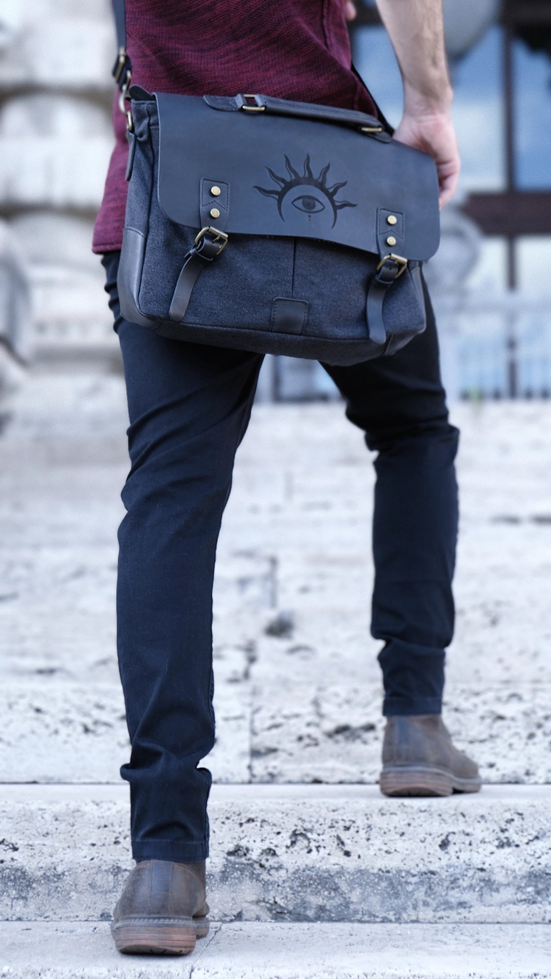 A model is wearing a black leather satchel engraved with a mystic eye with a solar crown. Dark academia style