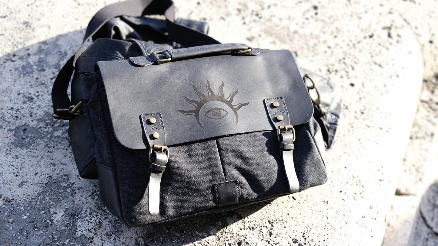 A black leather satchel engraved with a mystic eye with a solar crown. Dark academia style