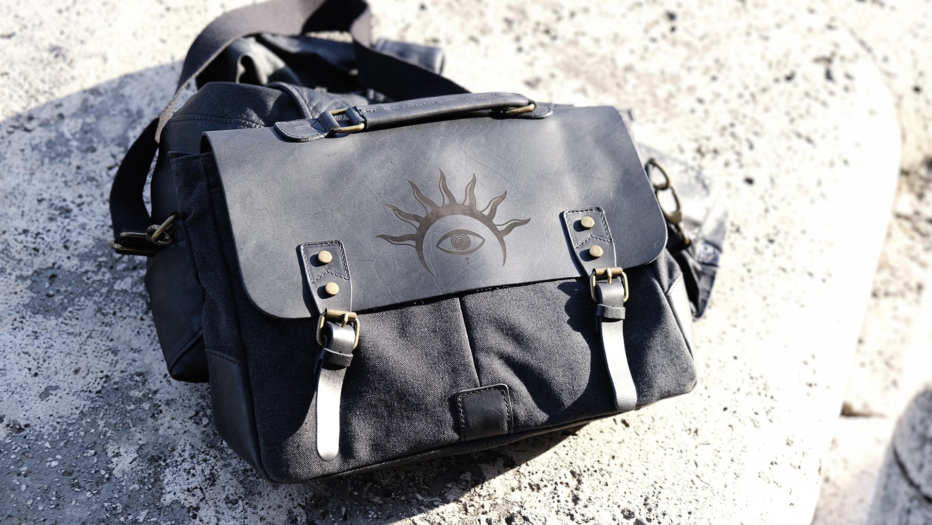 A black leather satchel engraved with a mystic eye with a solar crown. Dark academia style