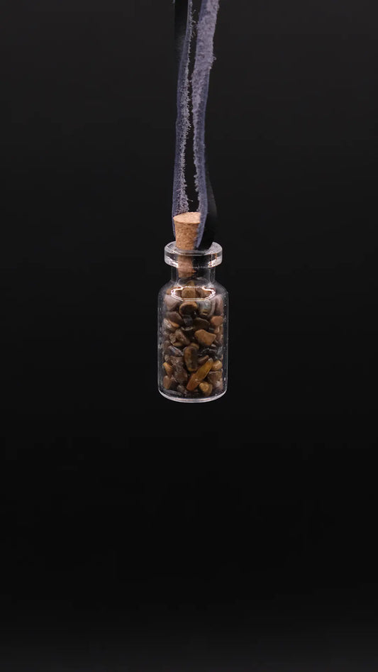 pendant made with a little glass bottle filled with tiger's eye shards placed over a black background
