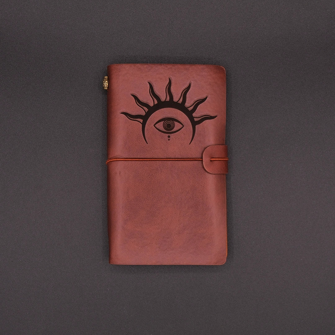 Brown, vegan leather vintage diary with an hermetic eye engraved on it, over a black background.