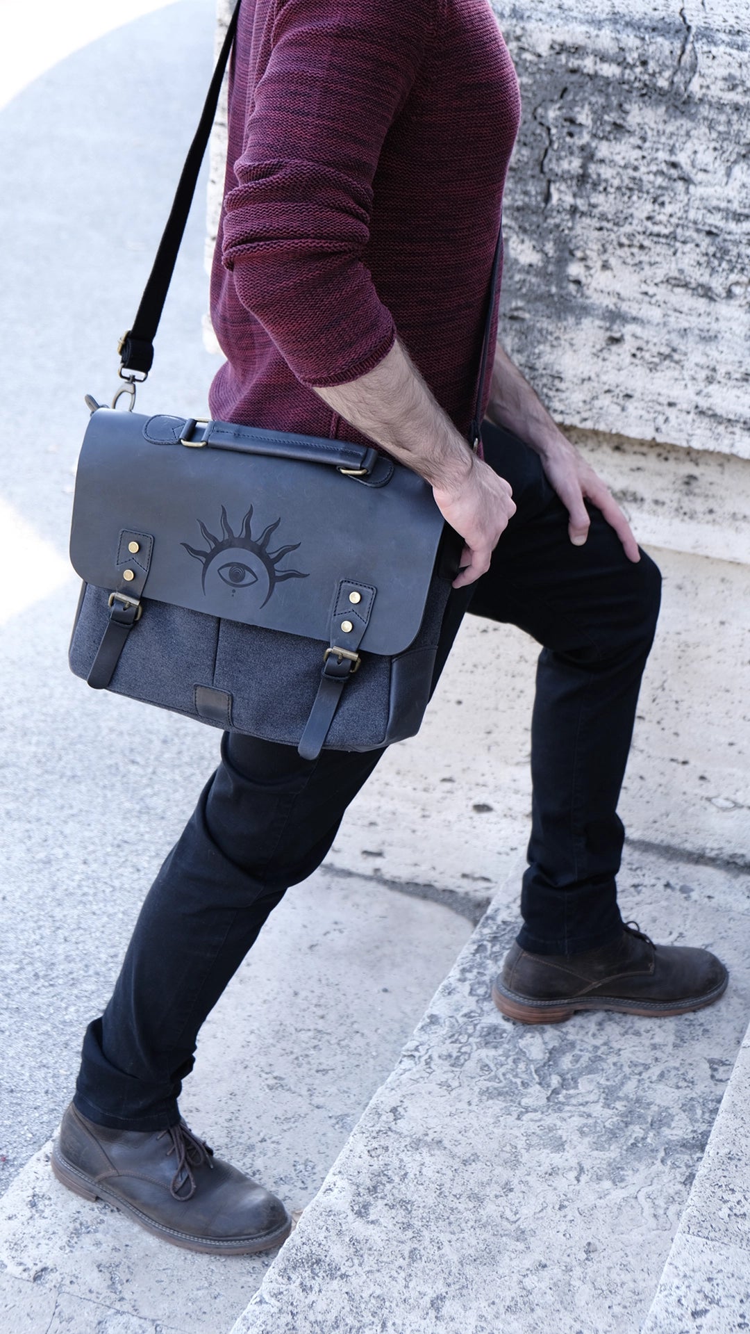 A model is wearing a black leather satchel engraved with a mystic eye with a solar crown. Dark academia style