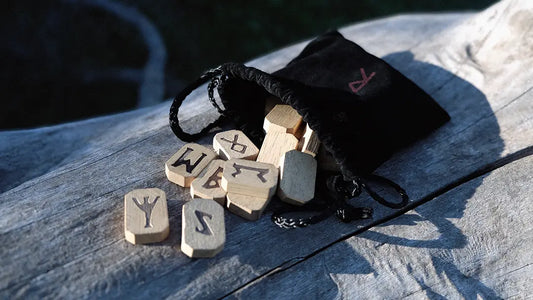 Black pleated bag with wooden runes on a wooden base.