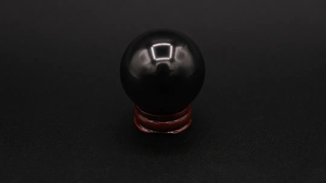 A perfect sphere made of black shungite stone, placed on a wooden stand over a black background