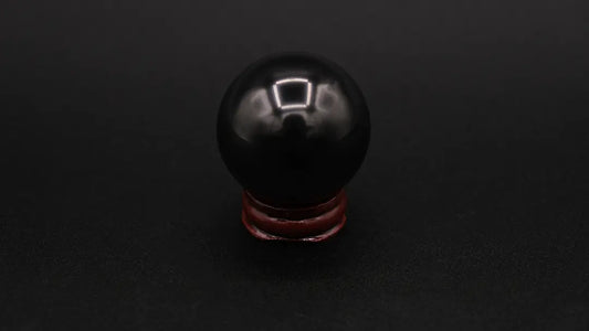 A perfect sphere made of black shungite stone, placed on a wooden stand over a black background
