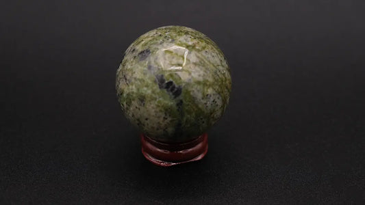 A perfect sphere made of green serpentine stone placed on a wooden stand over a black background