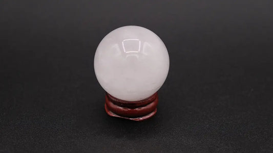 A perfect sphere made of white quartz, placed on a wooden stand over a black background