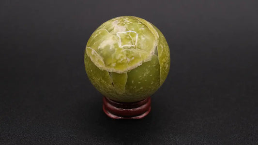 A perfect sphere made of yellow serpentine stone, placed on a wooden stand over a black background