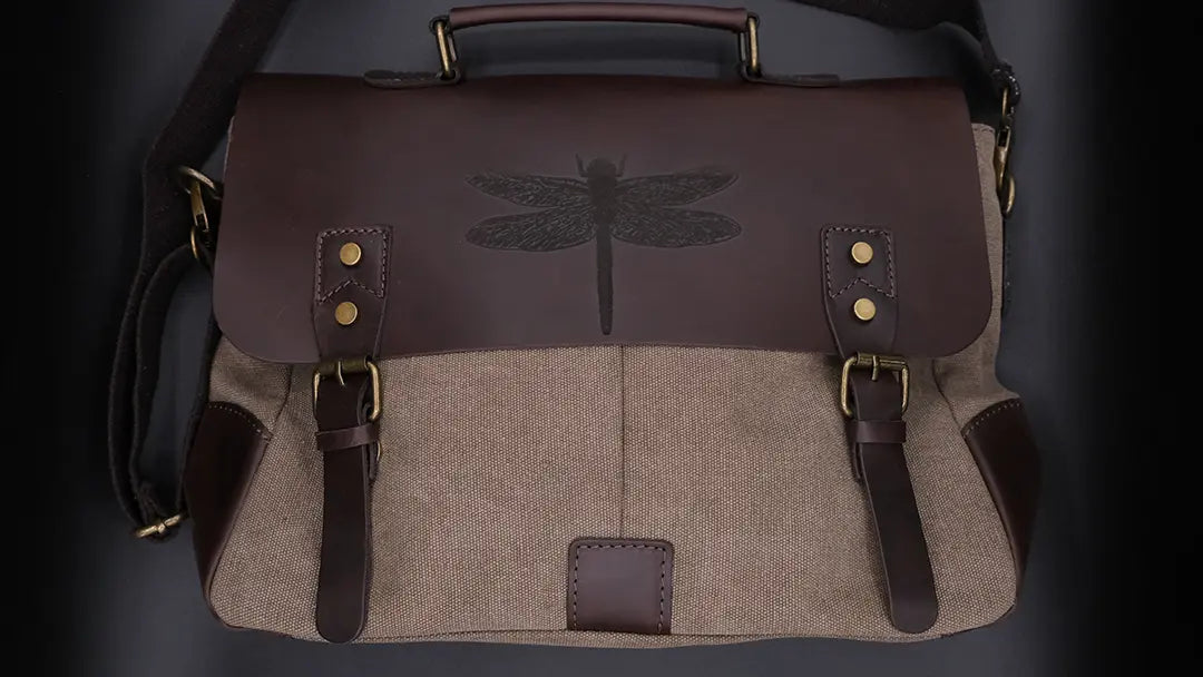 A brown leather satchel engraved with a dragonfly drawn is over a black background