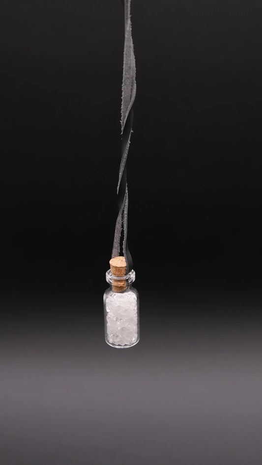 pendant made with a little glass bottle filled with white quartz shards placed over a black background