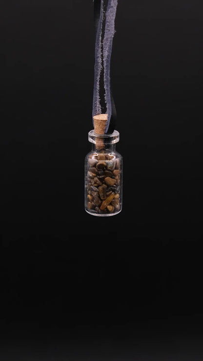 pendant made with a little glass bottle filled with tiger's eye shards placed over a black background