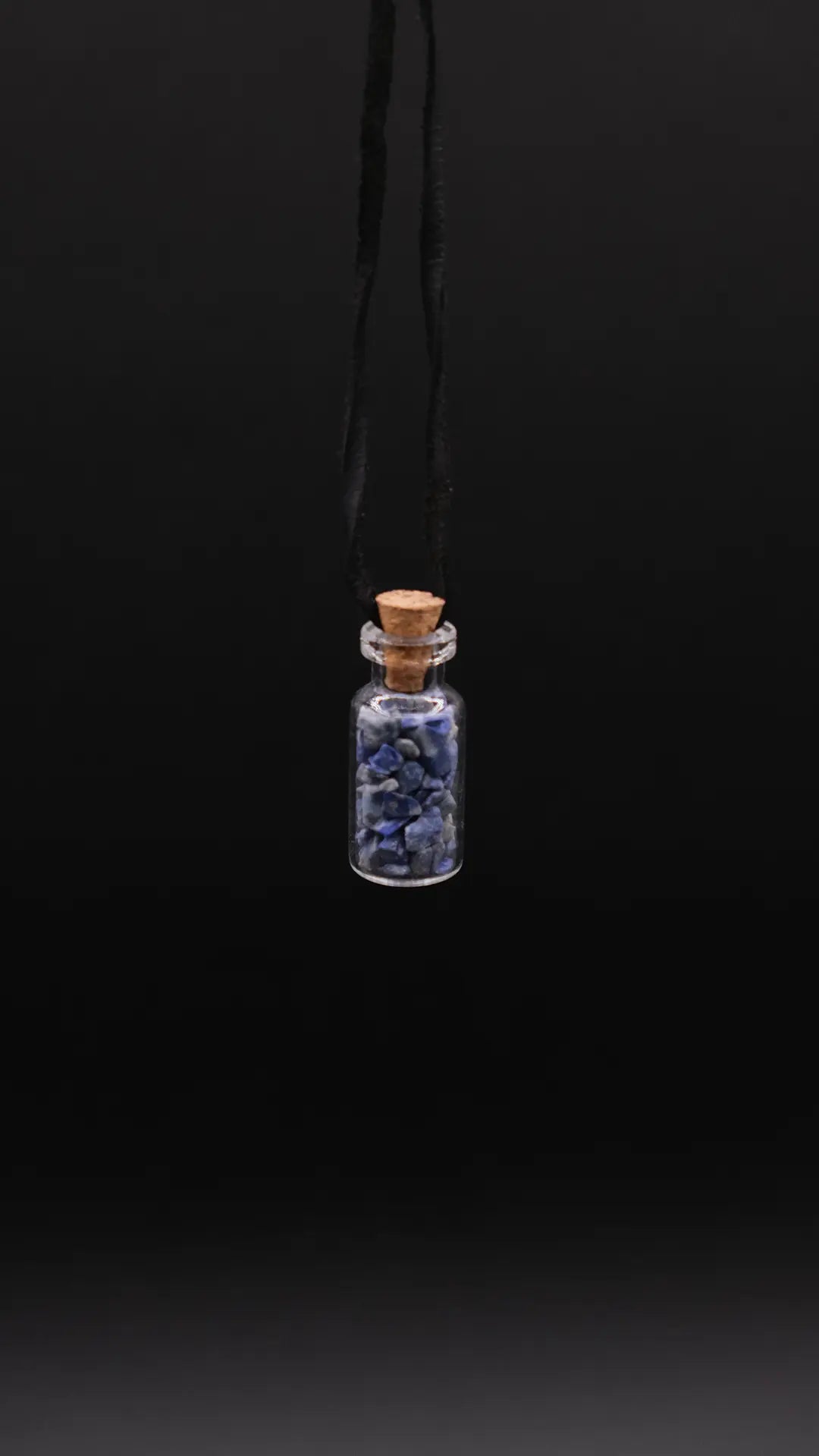 pendant made with a little glass bottle filled with lapis lazuli shards placed over a black background