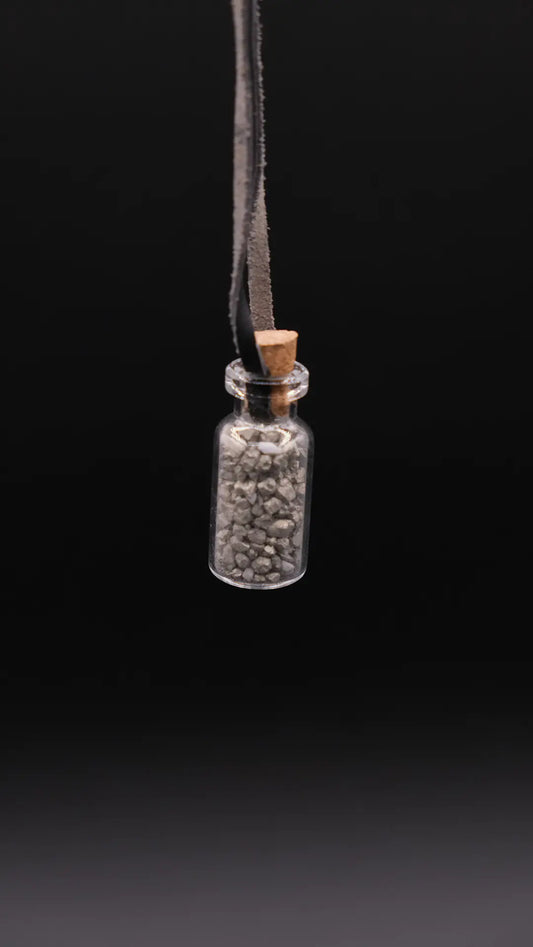 pendant made with a little glass bottle filled with pyrite shards placed over a black background