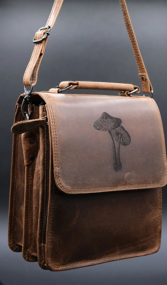 Shoulder bag in light brown leather with mushroom symbol engraved on the front , on the black background.